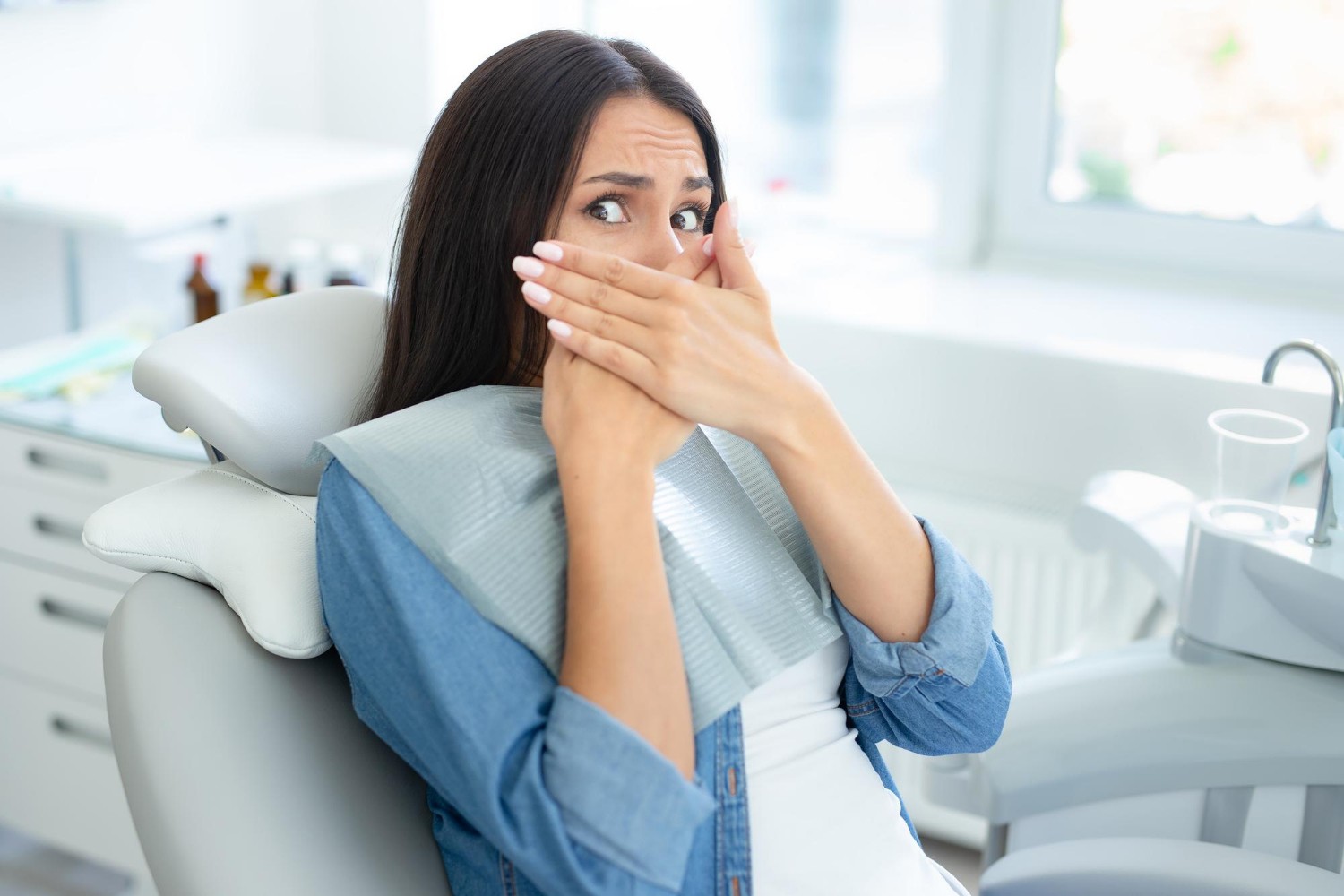 portrait of woman covering mouth with hands sirring in dental chair